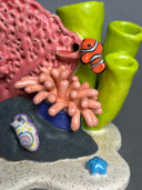 Ceramic sculpture of an under sea theme, with pink and green coral, a sea anemone, stones, fish and various other sea creatures.