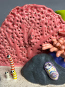 Ceramic sculpture of an under sea theme, with pink and green coral, a sea anemone, stones, fish and various other sea creatures.