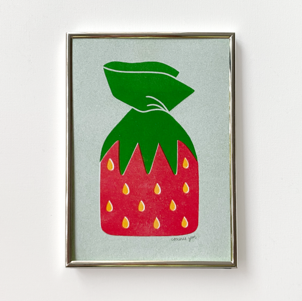 3 color risograph print in green, red and yellow of a piece of strawberry hard candy in its iconic strawberry wrapper. Background is light green and piece is in a thin metal frame.