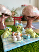 Set of several ceramic sculptures making up a picnic setting with 3 kappas dining outside on a plaid blanket with various Japanese food items and cups of green tea.
