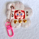 Glossy ceramic sculpture of a Tamagotchi toy with a pink cherry blossom shaped body and a small cherry blossom character inside. Gold gilded patterning and buttons are on the toy and it is attached to a chain.