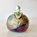 Ceramic sculpture of an apple with a small owl sitting on top, seen from the back with a pearlescent finishing of sorts.