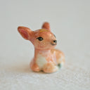 Sculpture of a small ceramic deer with a smiling face.