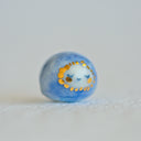 Small character ceramic sculpture of a orb with blue body and a tiny white face with gold cheeks and gold dots surrounding its face.