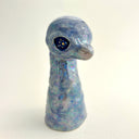 A small sculptural figurine shaped like a diplosaurus neck and head, covered in an iridescent blue, purple, and green glaze with gold foil flecks, photographed against a plain light background.