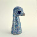 A small sculptural figurine shaped like a diplosaurus neck and head, covered in an iridescent blue, purple, and green glaze with gold foil flecks, photographed against a plain light background.