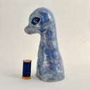 A small sculptural figurine shaped like a diplosaurus neck and head, covered in an iridescent blue, purple, and green glaze with gold foil flecks, photographed against a plain light background.