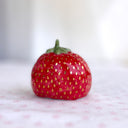 Small ceramic sculpture of a wide strawberry, shiny red with gold dots as seeds.