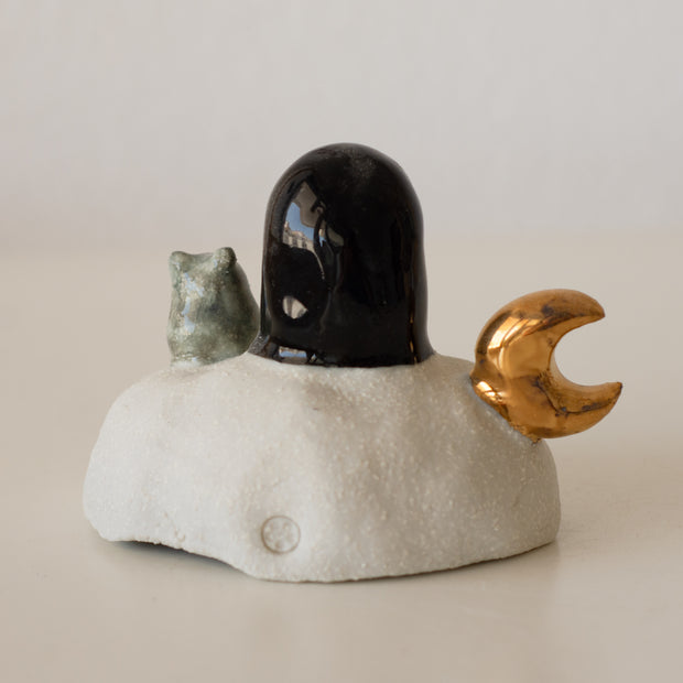 Ceramic sculpture of a No Face character sitting on a rock-like mound with a tiny mouse next to it and a golden moon on its other side.