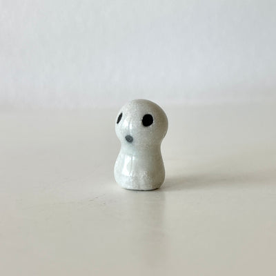 Small ceramic sculpture of a Kodama - a white forest spirit with a mostly shapeless body and a set of black eyes and a tiny "o" mouth.
