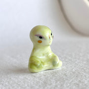 Small ceramic sculpture of a green alien, sitting in a meditation pose with crossed legs.
