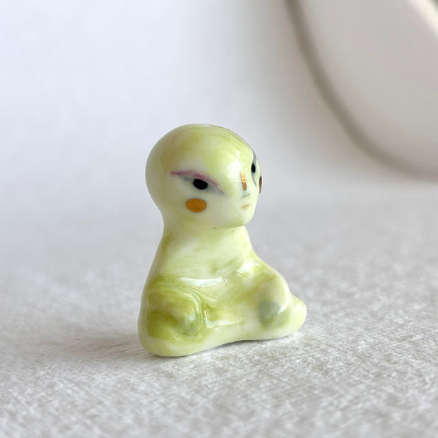 Small ceramic sculpture of a green alien, sitting in a meditation pose with crossed legs.