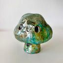 Raku fired ceramic sculpture of a piece of broccoli, with a cloud shaped top, a set of black eyes and a tiny stem for a body. 