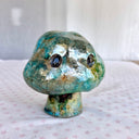 Raku fired ceramic sculpture of a piece of broccoli, with a cloud shaped top, a set of black eyes and a tiny stem for a body. 