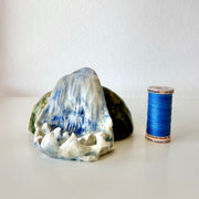 Ceramic sculpture of a waterfall over a rock. Sculpture is next to a spool of thread for size reference.