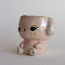 Shiny ceramic sculpture of a sitting cartoon bunny, with its head open and functional as a cup.