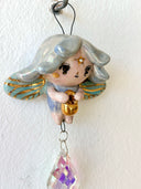 Hanging ceramic figure of a cartoon, cute fairy with wings and gold detailings. Hanging from her is a colorful crystal.