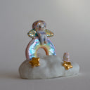 Small figurine of a fairy on a rainbow with stars and a very small pink bunny, all positioned on a fluffy cloud-like base. 