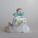 Small figurine of a fairy on a rainbow with stars and a very small pink bunny, all positioned on a fluffy cloud-like base. 