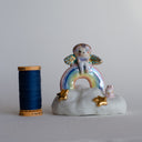 Small figurine of a fairy on a rainbow with stars and a very small pink bunny, all positioned on a fluffy cloud-like base. 
