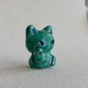 Green ceramic cat figurine designed to look like an alien with one of its paws up on a light gray surface
