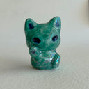 Green ceramic cat figurine designed to look like an alien with one of its paws up on a light gray surface