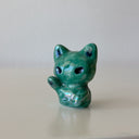 Green ceramic cat figurine designed to look like an alien with one of its paws up on a light gray surface