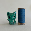 Green ceramic cat figurine designed to look like an alien with one of its paws up on a light gray surface