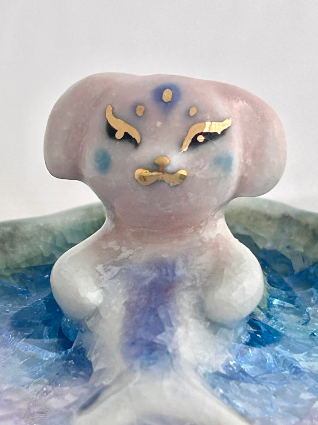 Ceramic sculpture of a creature that is half mermaid, half bunny, resting in a rounded body of water with a small gold crescent moon attached.