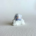 Small ceramic figurine of a circular character with small crystals all over it.