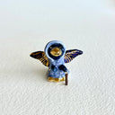 Tiny ceramic sculpture of a bird with a gold beak and gold and black wings, wearing a blue cloak and holding a small cane.