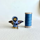 Tiny ceramic sculpture of a bird with a gold beak and gold and black wings, wearing a blue cloak and holding a small cane.