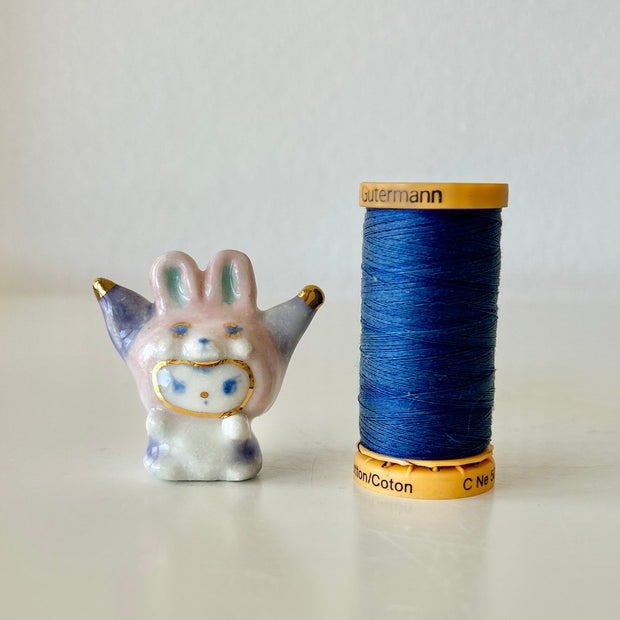 Small ceramic rabbit figure next to a spool of blue thread on a light background
