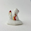 Small ceramic figurine of a white fox with red and gold color accents, sitting atop of a cloud like shape.
