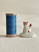 Small ceramic figurine of a white fox with red and gold color accents, sitting atop of a cloud like shape.