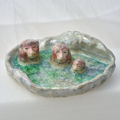 Ceramic dish made to look like a circular onsen in the snow with 3 monkeys bathing in it.