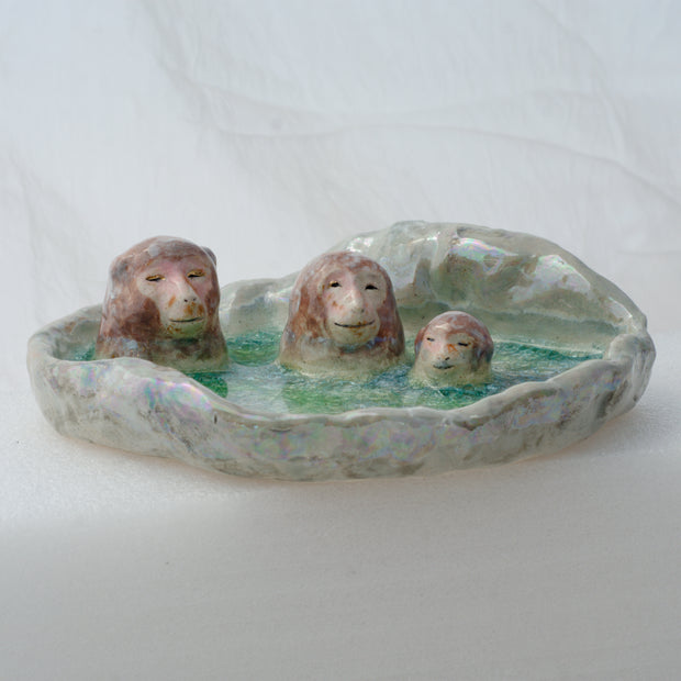 Ceramic dish made to look like a circular onsen in the snow with 3 monkeys bathing in it.