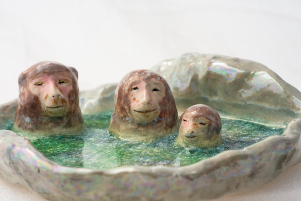 Ceramic dish made to look like a circular onsen in the snow with 3 monkeys bathing in it.