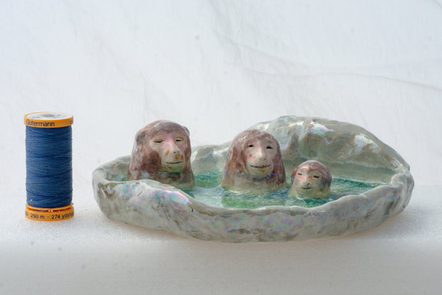 Ceramic dish made to look like a circular onsen in the snow with 3 monkeys bathing in it.