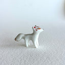 Small ceramic sculpture of a white fox with red and gold detail coloring.