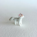 Small ceramic sculpture of a white fox with red and gold detail coloring.