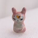 Pink rabbit figurine with a yellow heart on its forehead. It sits on a light pink background
