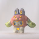 Ceramic white bunny figurine with a pink bunny hood hat with gold and green accents on a light gray background