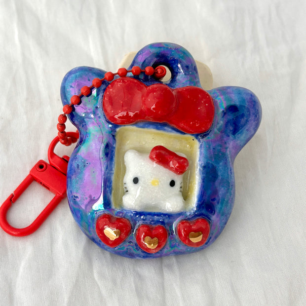 Hello Kitty-themed keychain with a red bow and purple frame on a white background