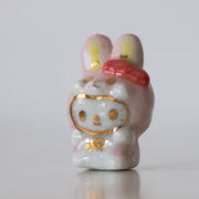 Ceramic figurine with a cartoon face and pink hair bow on a white background