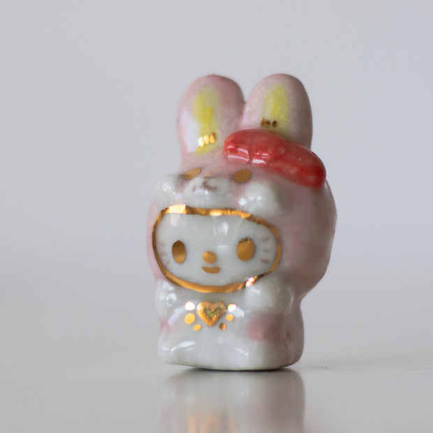 Ceramic figurine with a cartoon face and pink hair bow on a white background