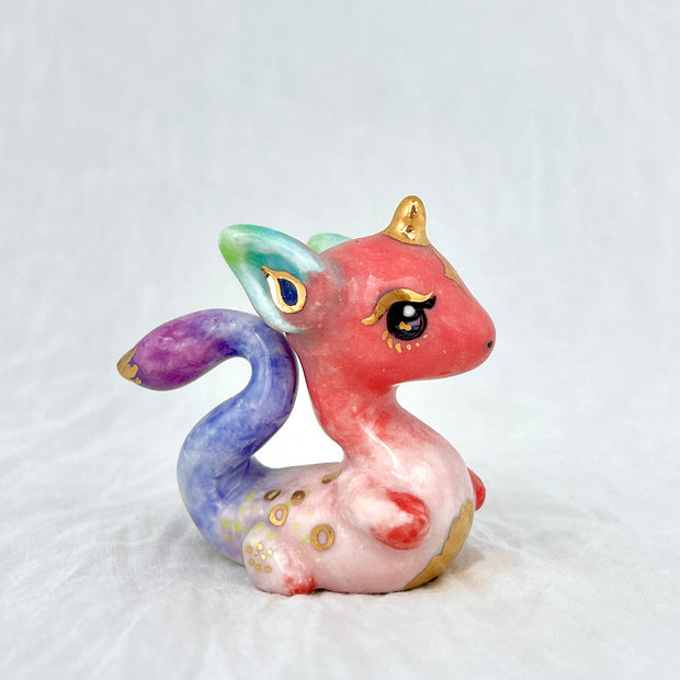 Colorful dragon-like figurine with pink body, purple tail, and gold accents on a light gray background