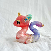 Colorful dragon figurine with pink, purple, and gold accents on a white background