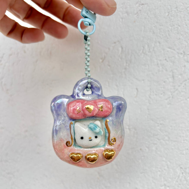 Ceramic sculpture of a Tamagotchi with gold buttons and a Hello Kitty like character in the screen.