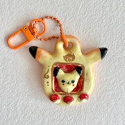 Ceramic keychain sculpture of a Pikachu themed tamagotchi, with an orange keychain and buttons that are like pokeballs.